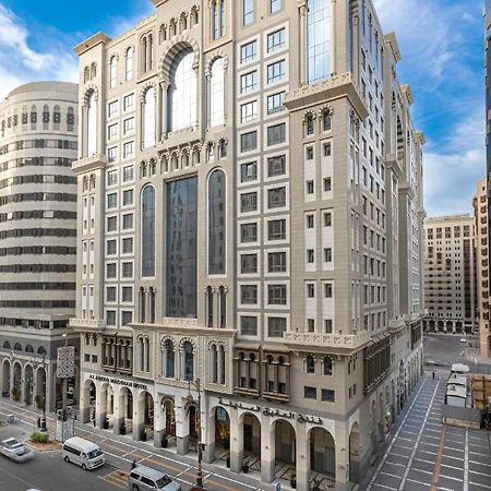 Al Aqeeq Madinah Hotel マディーナ エクステリア 写真 The photo depicts a large, modern building with a distinctive architectural style. The structure shows a blend of classic and contemporary design elements, featuring ornate details, large glass windows, and a prominent central facade. Surrounding the