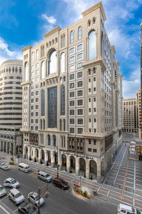 Al Aqeeq Madinah Hotel マディーナ エクステリア 写真 The photo depicts a large, modern building with a distinctive architectural style. The structure shows a blend of classic and contemporary design elements, featuring ornate details, large glass windows, and a prominent central facade. Surrounding the