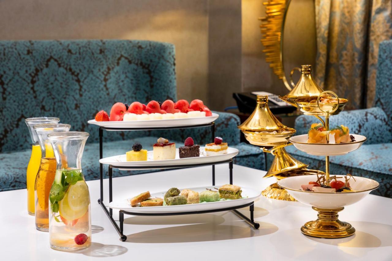 Al Aqeeq Madinah Hotel マディーナ エクステリア 写真 The photo displays an elegant dessert arrangement on a table. There are two levels of desserts: 

1. **Top Tier**: Features a selection of colorful sweets, including layers of cream or mousse desserts, garnished with fresh berries.
2. **Bottom Tier**