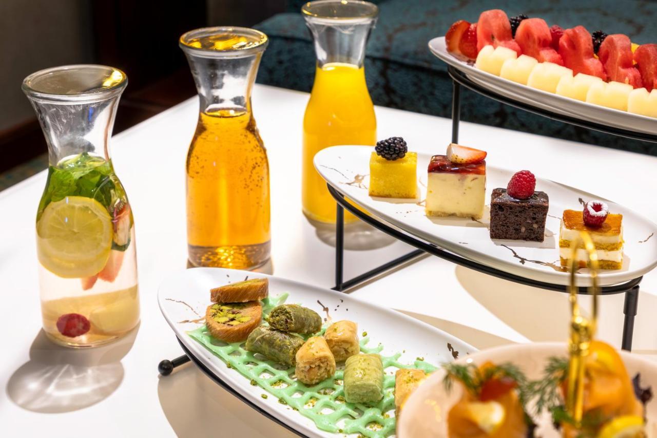 Al Aqeeq Madinah Hotel マディーナ エクステリア 写真 The photo showcases an elegant display of refreshments and desserts. There are several glass pitchers filled with bright, colorful beverages, likely juices or infused water, one featuring lemon and mint. A two-tier serving stand holds an assortment o