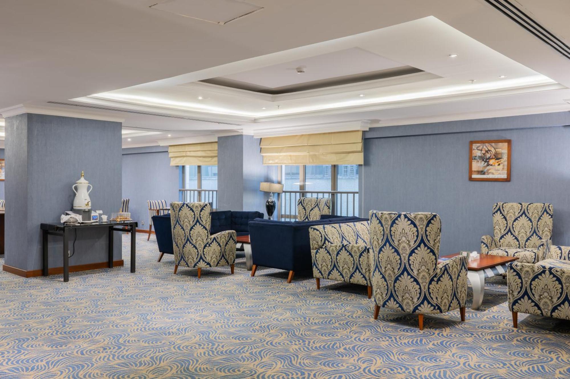 Al Aqeeq Madinah Hotel マディーナ エクステリア 写真 The photo shows a stylish indoor lounge or sitting area. It features several upholstered armchairs arranged around a central space. The chairs have a blue and cream patterned upholstery, creating a sophisticated ambiance. There is a table alongside s