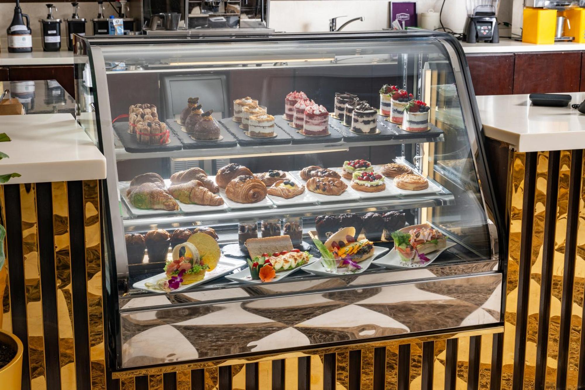 Al Aqeeq Madinah Hotel マディーナ エクステリア 写真 The photo shows a display case filled with an assortment of desserts. There are various types of pastries, including cakes, tarts, and croissants, arranged neatly on different shelves. The desserts are visually appealing, with colorful decorations, f