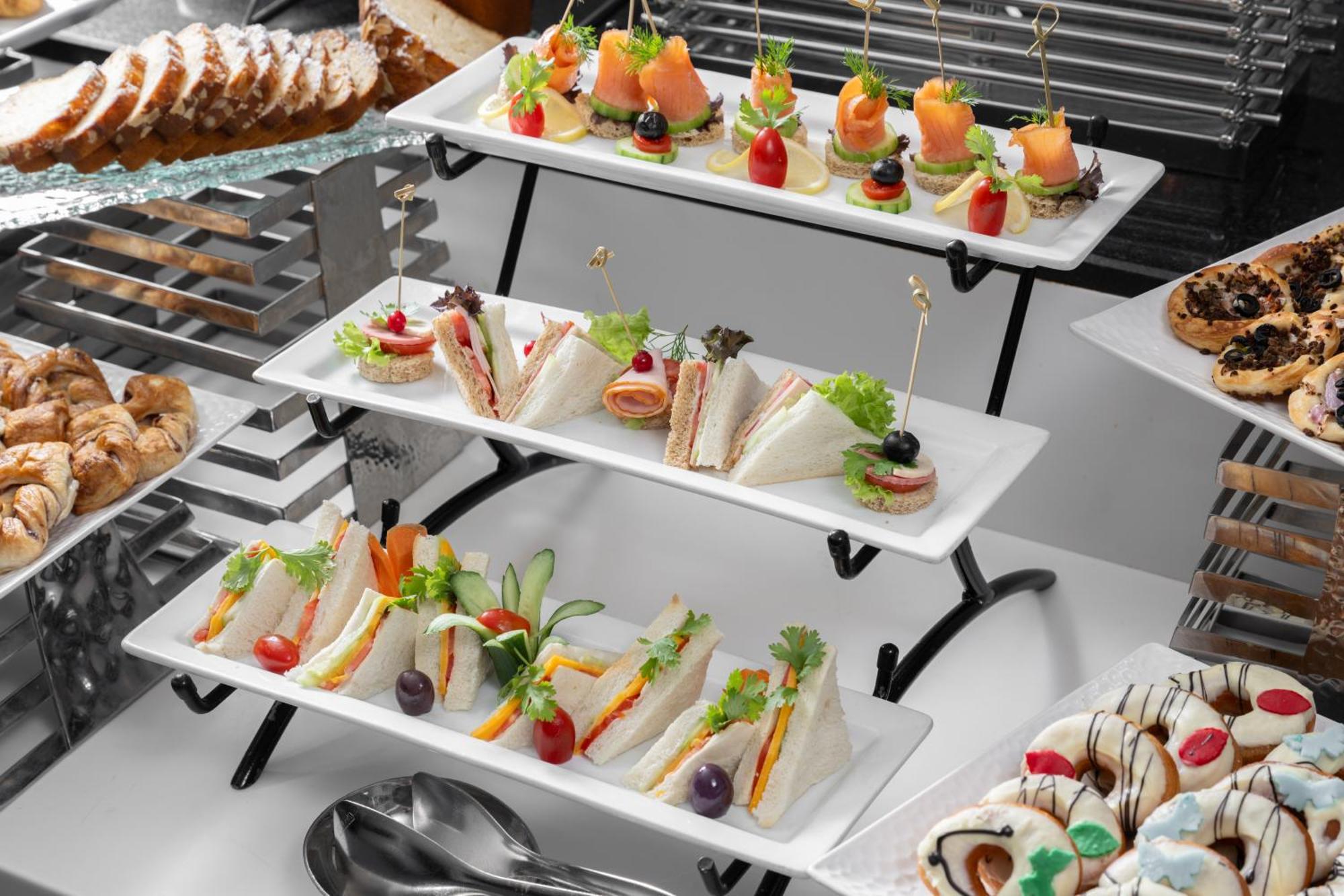 Al Aqeeq Madinah Hotel マディーナ エクステリア 写真 The photo shows a tiered display of assorted appetizers and snacks arranged on white rectangular plates. 

1. **Top Tier**: Contains small bites featuring smoked salmon garnished with greenery, and some with colorful cherry tomatoes on toothpicks. 

