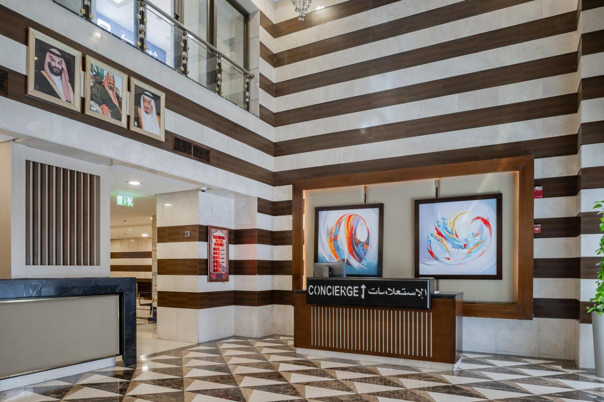 Al Aqeeq Madinah Hotel マディーナ エクステリア 写真 The photo shows a modern hotel lobby area characterized by its stylish design. The walls feature a pattern of horizontal stripes in different shades, creating a sophisticated atmosphere. To the left, there is a reception area with a sleek desk labele