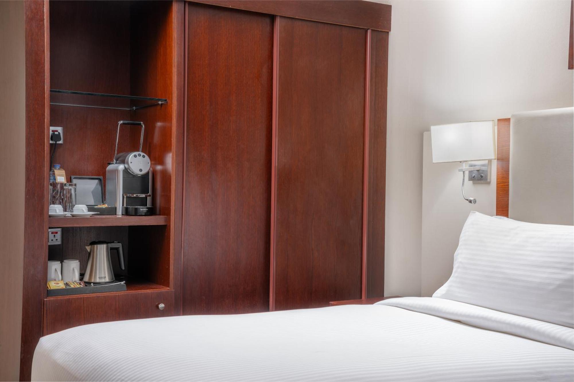 Al Aqeeq Madinah Hotel マディーナ エクステリア 写真 The photo shows a hotel room with a minimalist design. On the left side, there's a wooden cabinet with sliding doors that houses a small coffee maker and additional amenities, such as cups and a kettle. The bed is neatly made with white bedding and i