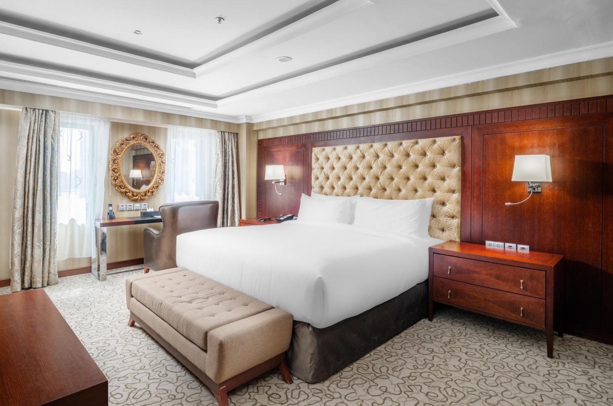 Al Aqeeq Madinah Hotel マディーナ エクステリア 写真 The photo shows a well-furnished hotel room featuring a large bed with a tufted headboard. The room has a warm color palette with wooden accents and soft lighting. There are two windows with curtains that allow natural light to fill the space. Alongs