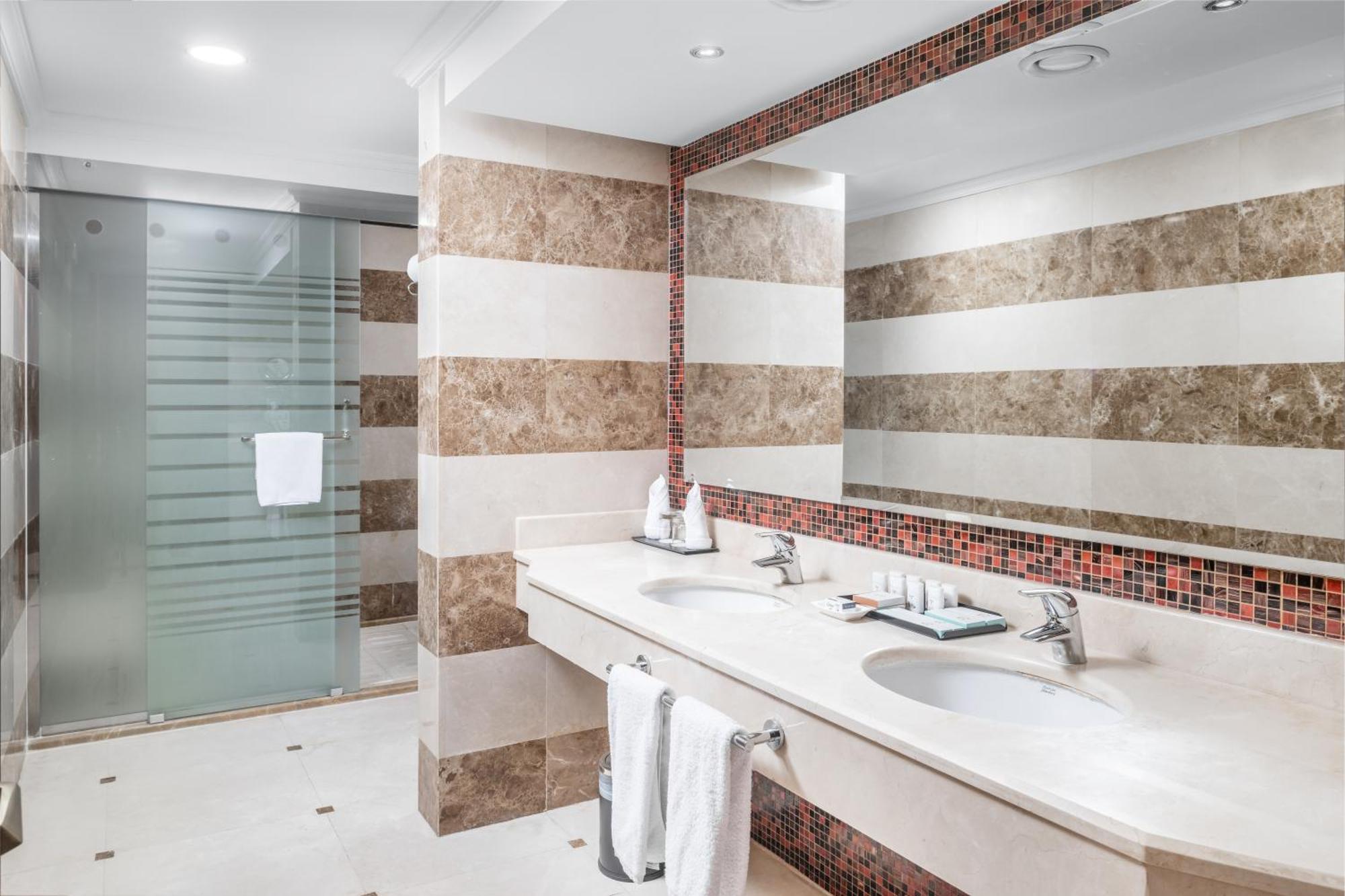 Al Aqeeq Madinah Hotel マディーナ エクステリア 写真 The photo shows a modern bathroom with an elegant design. It features a large double sink with a smooth countertop, accompanied by faucets. The walls are adorned with alternating horizontal stripes of light and dark materials, creating a stylish look
