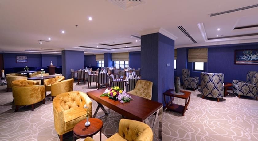 Al Aqeeq Madinah Hotel マディーナ エクステリア 写真 The photo shows a stylish interior of a restaurant or dining area. It features elegantly arranged seating with plush, gold-colored chairs and a wooden table at the center, adorned with a floral arrangement. The background includes more dining tables,