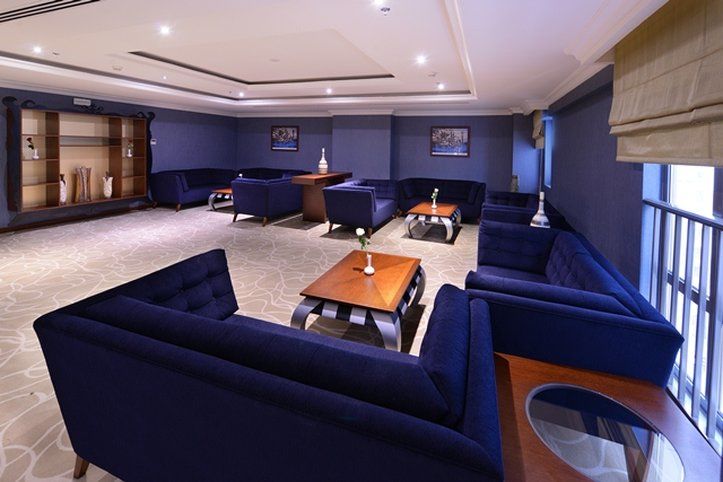 Al Aqeeq Madinah Hotel マディーナ エクステリア 写真 The photo shows a modern lounge area featuring a sophisticated design. The room is painted in a deep blue color, creating a calm and elegant atmosphere. There are several dark blue sofas arranged around a central wooden coffee table. The table is dec