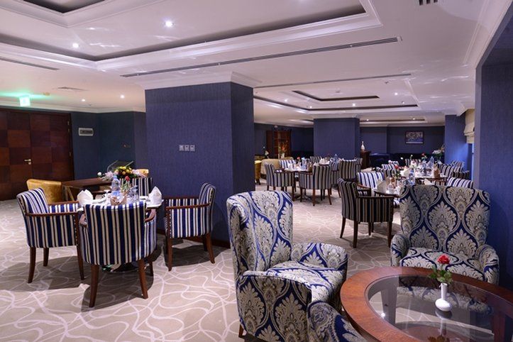 Al Aqeeq Madinah Hotel マディーナ エクステリア 写真 The photo shows an elegant dining or lounge area. The space features plush seating with striped and patterned chairs, and tables set up for dining. The decor includes a rich color palette with blue walls and soft lighting creating a warm atmosphere. 