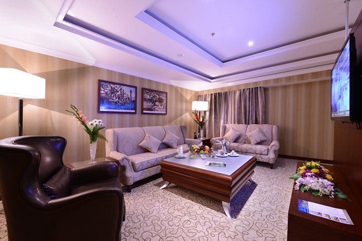 Al Aqeeq Madinah Hotel マディーナ エクステリア 写真 The photo shows a stylish and comfortable living room. It features two light-colored sofas with decorative cushions arranged around a modern coffee table. In one corner, there's a dark, leather armchair. The walls are adorned with framed artwork, and