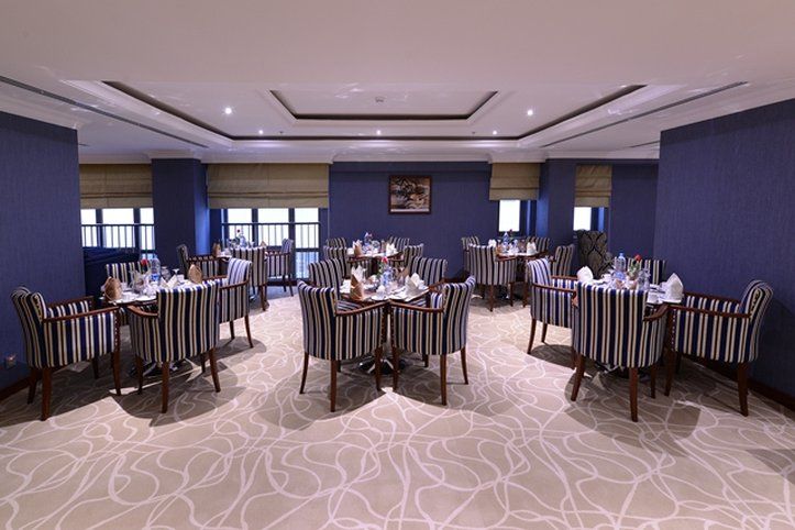 Al Aqeeq Madinah Hotel マディーナ エクステリア 写真 The photo shows an elegant dining room equipped with several tables. Each table is set with white tableware and neatly arranged silverware, giving a formal dining appearance. The decor features striped chairs and a carpet with a subtle pattern. The w