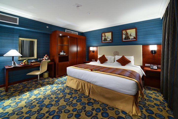 Al Aqeeq Madinah Hotel マディーナ エクステリア 写真 The photo shows a hotel room designed with a modern and stylish aesthetic. It features a large bed with a cream-colored headboard and decorative pillows. The room is decorated with blue walls and patterned carpet, creating a cozy atmosphere. 

There 