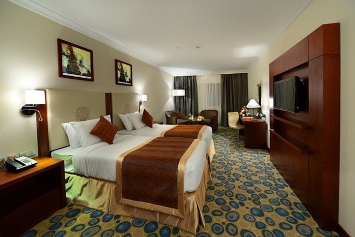 Al Aqeeq Madinah Hotel マディーナ エクステリア 写真 The photo shows a hotel room featuring two beds with white linens and brown throw blankets. There are decorative pillows on the beds. The room has a modern design, with wooden furniture including bedside tables and a large wooden unit that houses a t